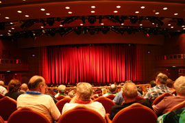 Photo of audience in theatre with lighted stage curtain.